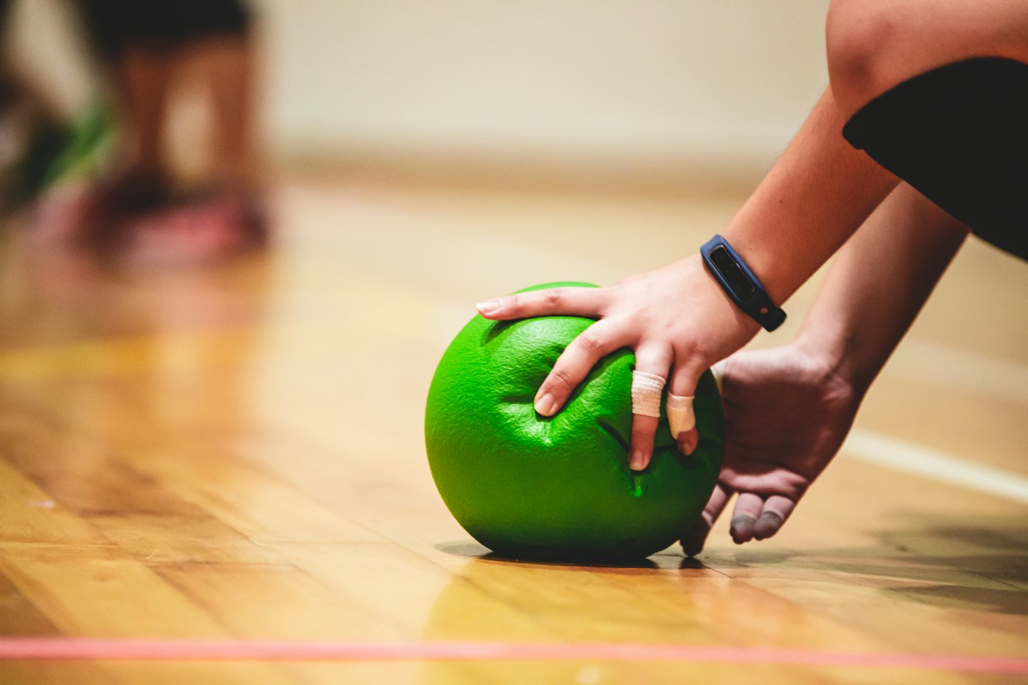Manos presionando una pelota de dodgeball verde brillante en el suelo de un gimnasio.